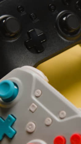 Vertical-Video-Studio-Close-Up-Of-Two-Video-Game-Controllers-On-Yellow-Background